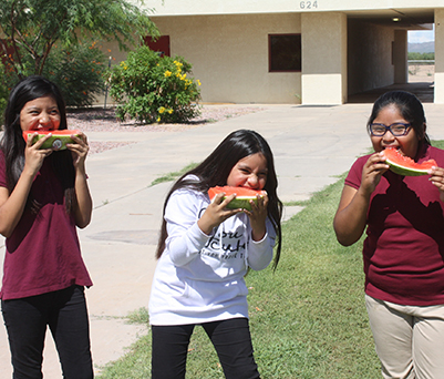 Three happy girls eating watermelon outside at school