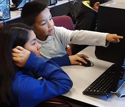 Two elementary students helping each other while working on a computer